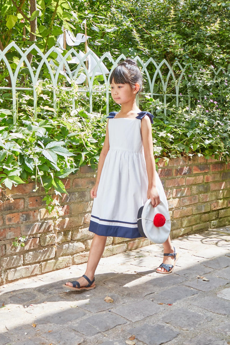 Sidonie, pinafore dress with contrasting strap with bows and navy  bands at the bottom, in White cotton piqué