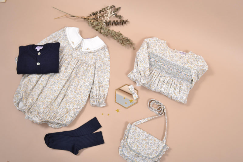 Véra, Barboteuse bébé fille manches longues, double col volanté, taille smockée, imprimé fleuri bleu ciel/moutarde - Véra, Baby girl's long-sleeved romper, double ruffled collar, smocked waist, in Sky blue/mustard floral print