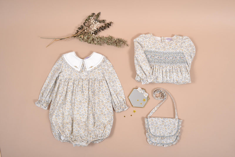 Véra, Barboteuse bébé fille manches longues, double col volanté, taille smockée, imprimé fleuri bleu ciel/moutarde - Véra, Baby girl's long-sleeved romper, double ruffled collar, smocked waist, in Sky blue/mustard floral print